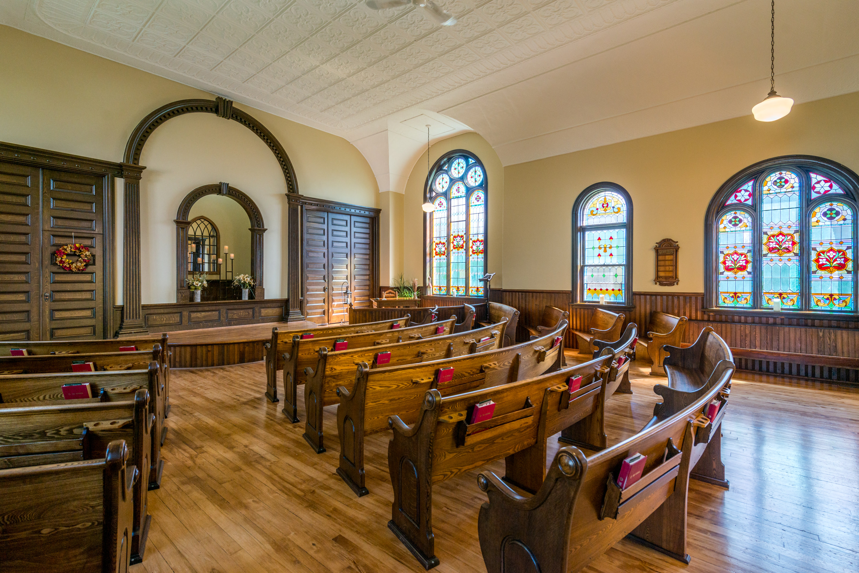 Interior photo of rows of wooden pews, several stained glass windows, and beautifully maintained hardwood floors.